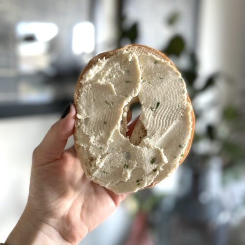 Hand holding bagel topped with vegan chive & onion cream cheese